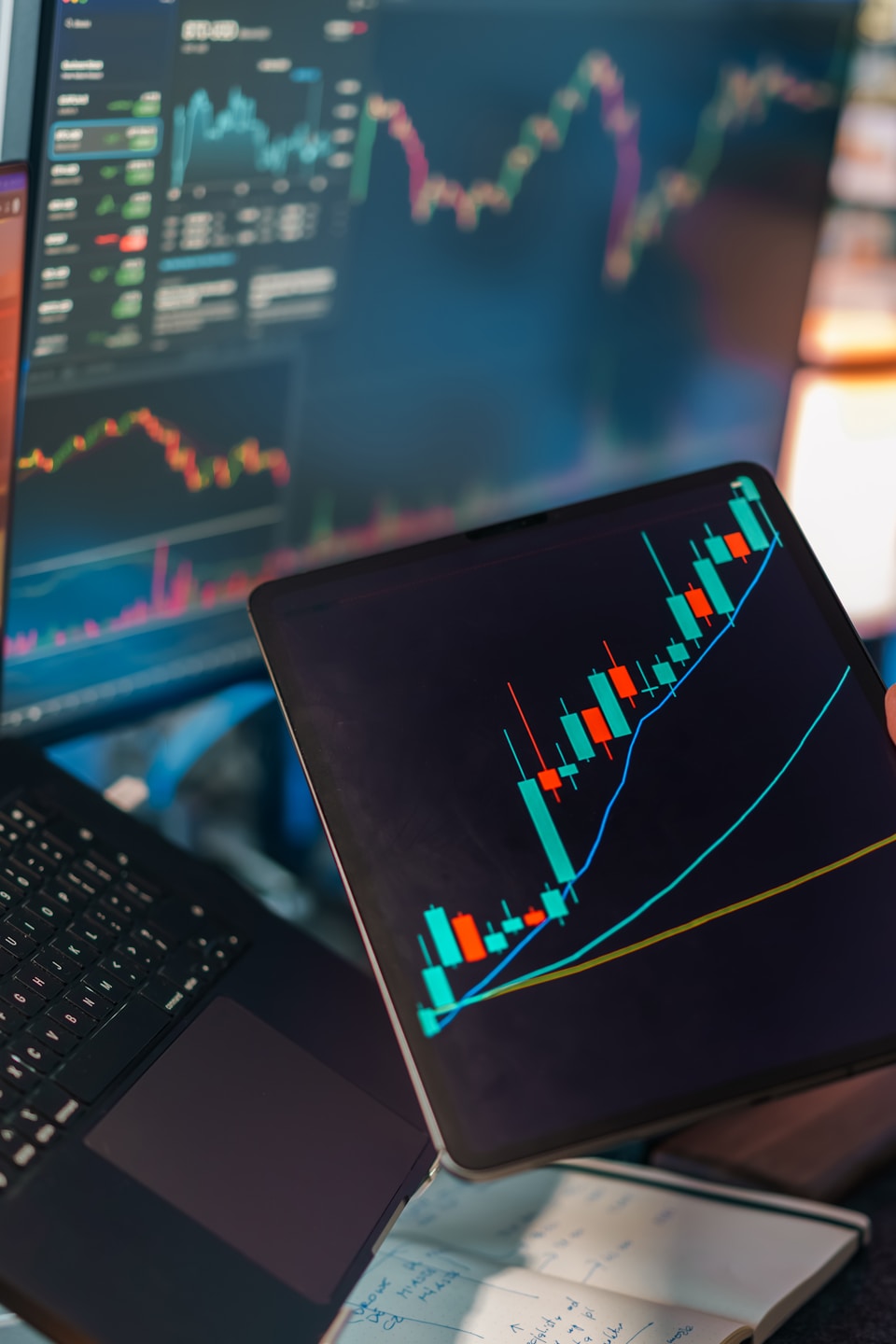 Trading charts displayed on multiple screens and tablet.
